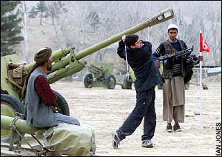 The Daily Telegraph's Peter Foster playing an iron is watched over by his  armed  caddie, Abdul Qayum, next to 75 mm Russian howitzers